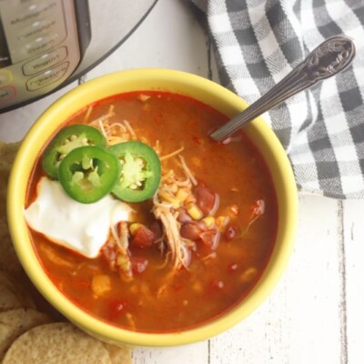 Mexican tortilla soup topped with sour cream and jalapenos in a yellow bowl next to tortilla chips and an instant pot.