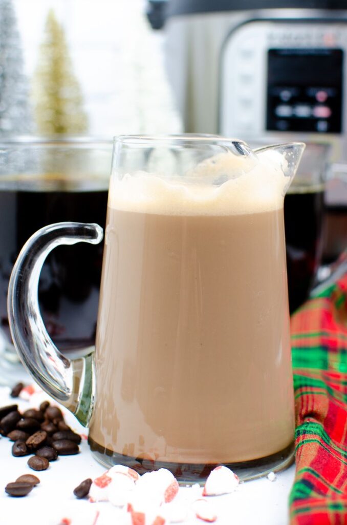 Instant Pot Peppermint Mocha Creamer and coffee in a glass mug next to peppermints, coffee beans, and a green and red cloth  with coffee in glass mugs and an instant pot in the background
