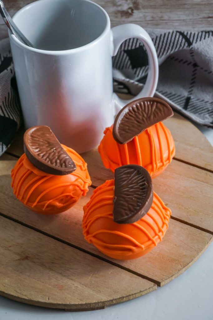 Chocolate Orange Hot Cocoa Bombs next to a white mug on wooden platter