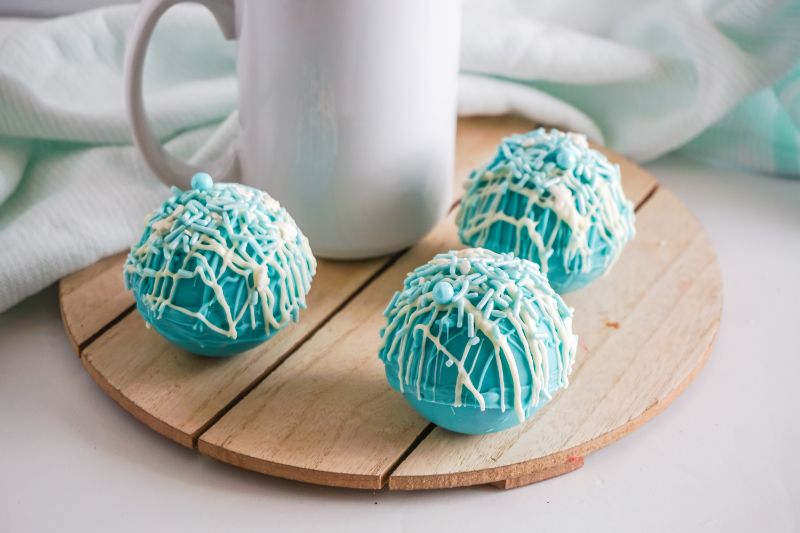 Frozen Hot Cocoa Bombs with white mug on wooden platter