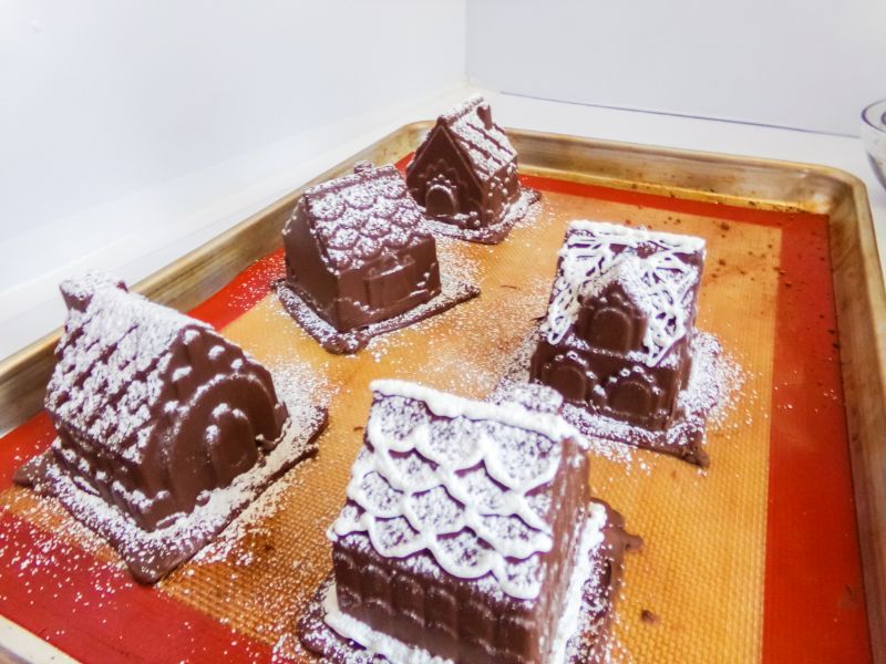 powdered sugar on top of the chocolate gingerbread house cocoa bombs