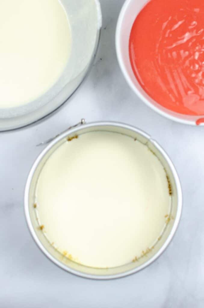 Parchment lined cake tin next to a mixture of red velvet cheesecake mix.