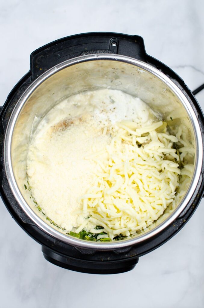 Different cheese on top of spinach artichoke dip in an instant pot.