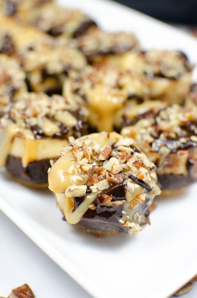 Pecan and caramel covered instant pot mini turtle cheesecakes on a white plate.