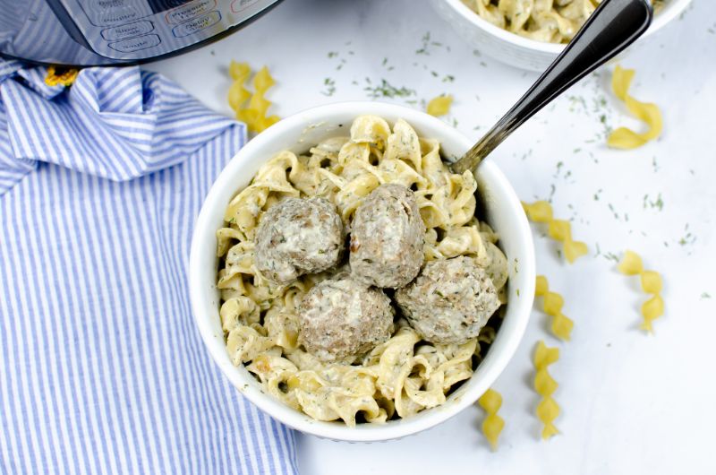 Swedish meatballs and egg noodles in a white bowl with a spoon.
