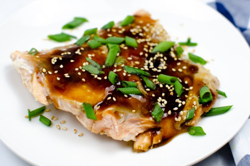 Baked salmon in Teriyaki Sauce on a white plate garnished with sesame seeds and green onions.