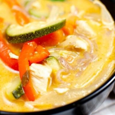Thai red chicken curry in a black bowl with red peppers and zucchini on top.