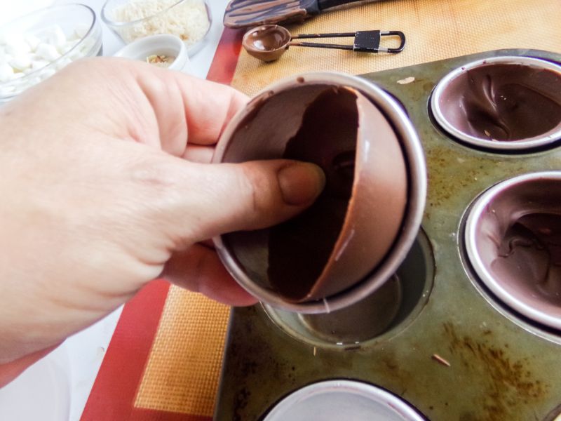 a hand taking out the hardened chocolate shell from the mold with more molds underneath in a pan