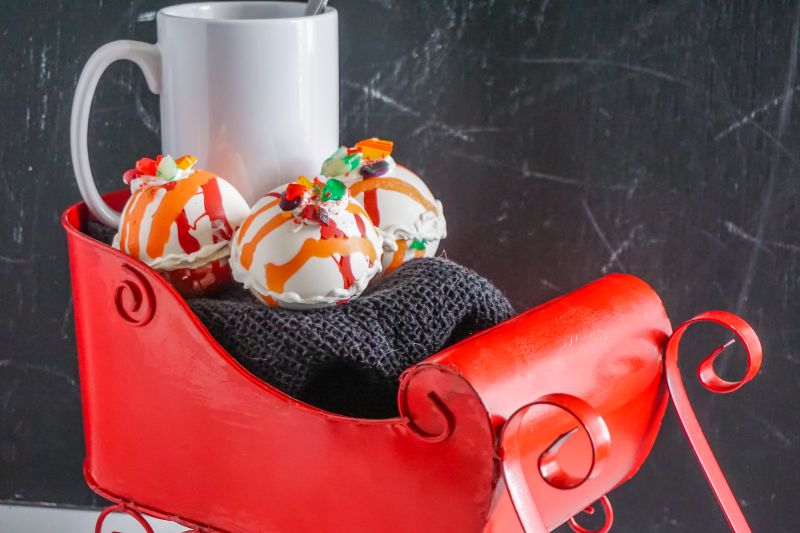 hot cocoa bombs next to a white mug in red sleigh