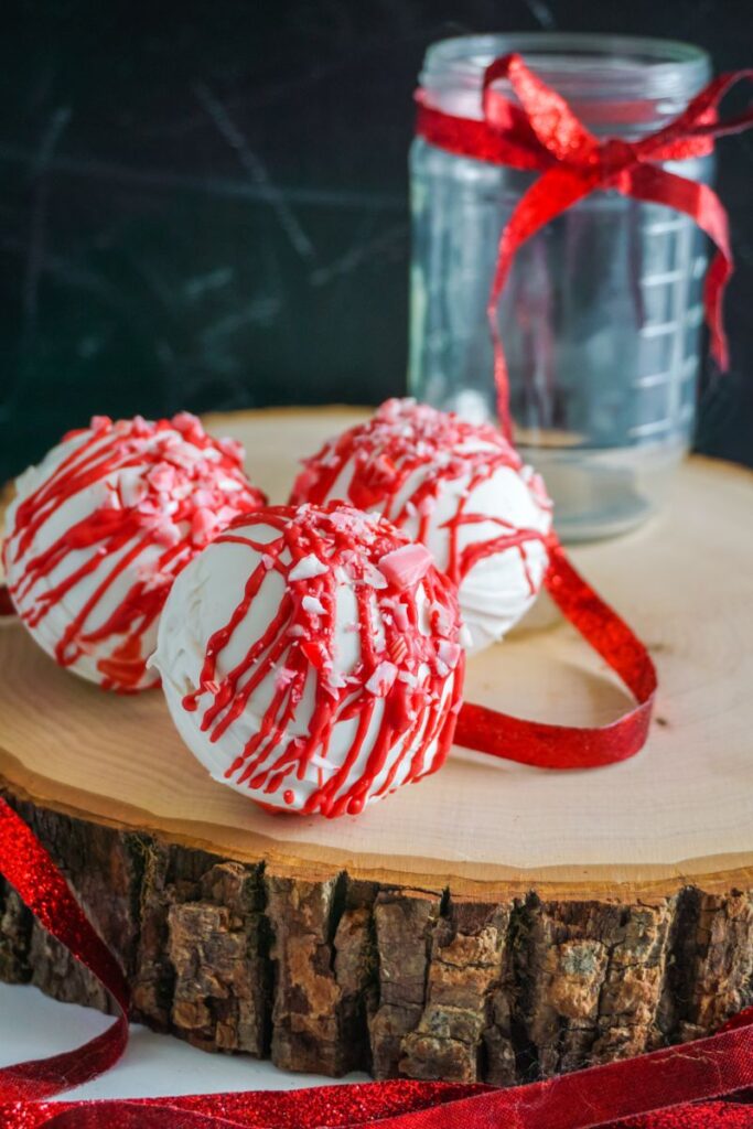 Peppermint Hot Cocoa Bombs on wooden platter  next to a glass jar with a red ribbon on it
