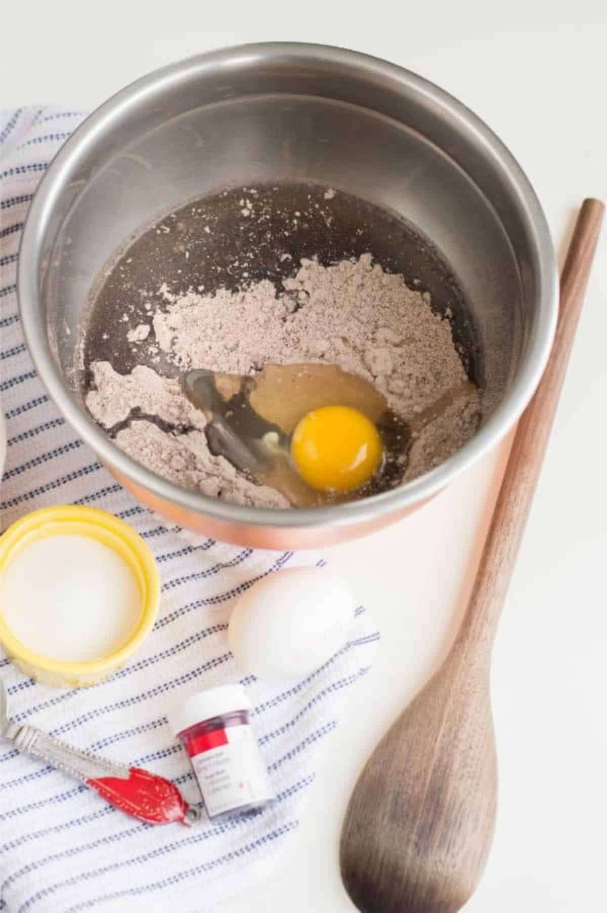 cake mix, oil and eggs in a mixing bowl next to a wooden spoon and other ingredients.