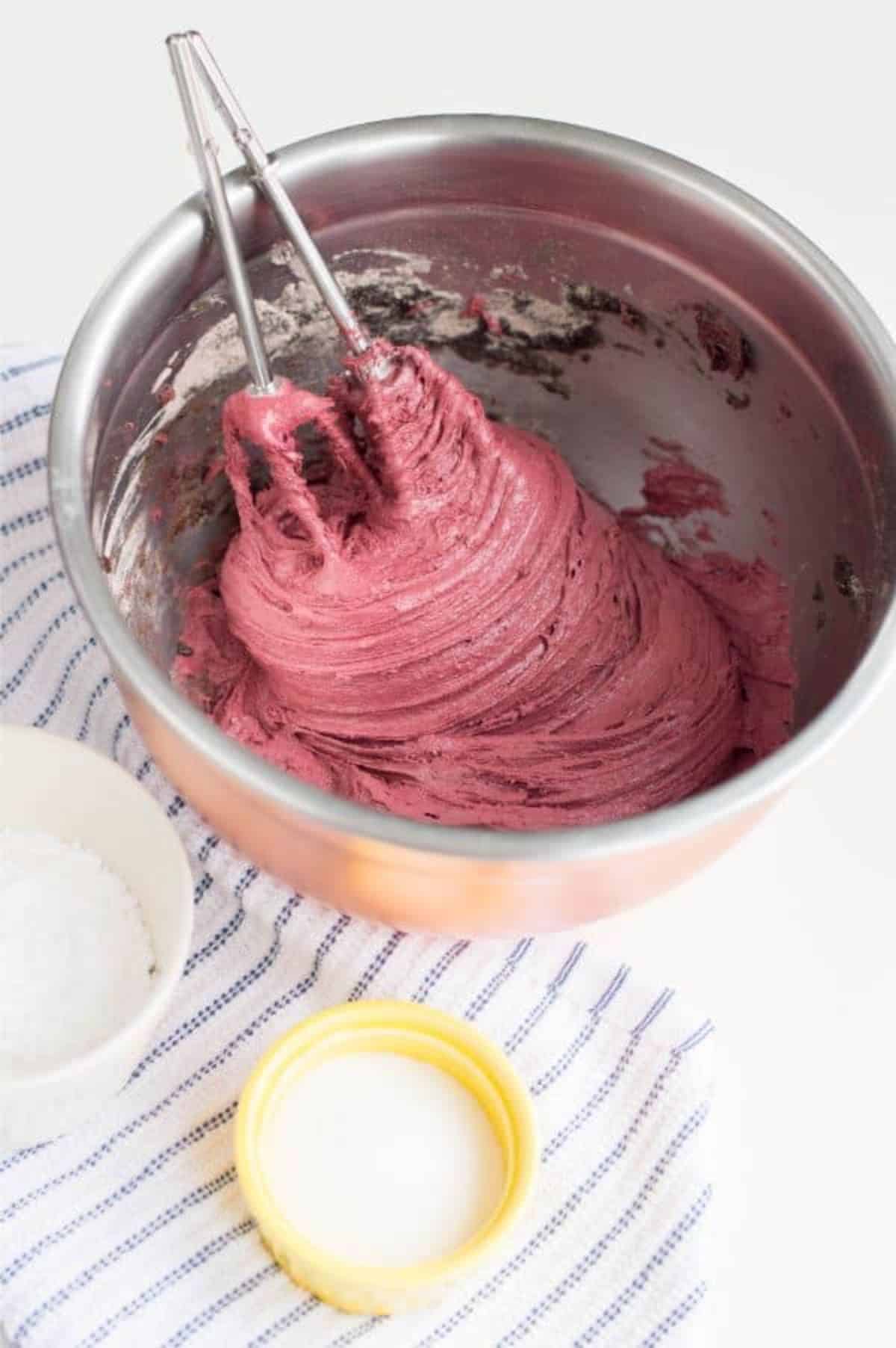 chocolate cake mix mixed with red gel food coloring in a stainless mixing bowl with beaters in it.