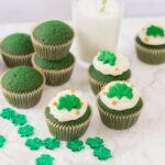 a dozen green velvet cupcakes with a glass of milk