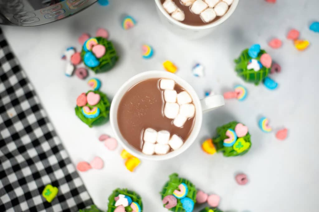 Instant Pot St. Patrick’s Day Hot Cocoa Bombs in mug that turned into hot chocolate with more hot cocoa bombs next to it on a white table