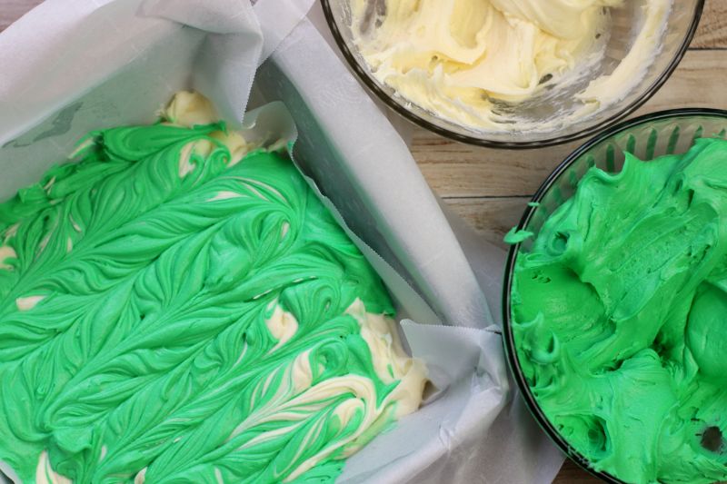 swirled white and green fudge in a pan next to bowls of the fudge