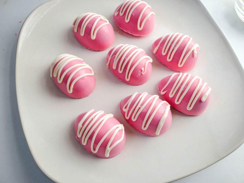 pink hot cocoa bombs with drizzled white frosting on a white plate