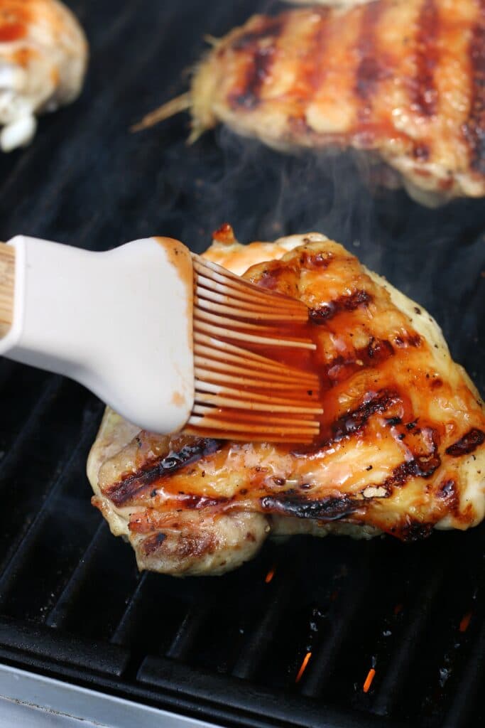 adding BBQ sauce to chicken on the grill 