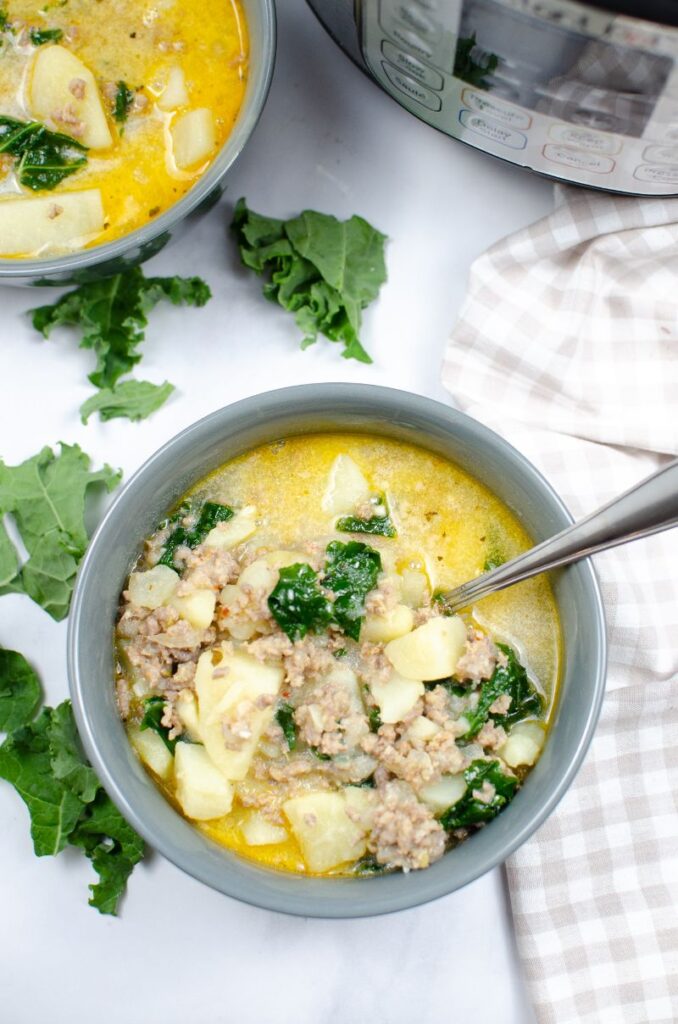 overhead view of Instant Pot Zuppa Toscana soup in a bowl with a spoon in it with another bowl of soup and an instant pot in the background
