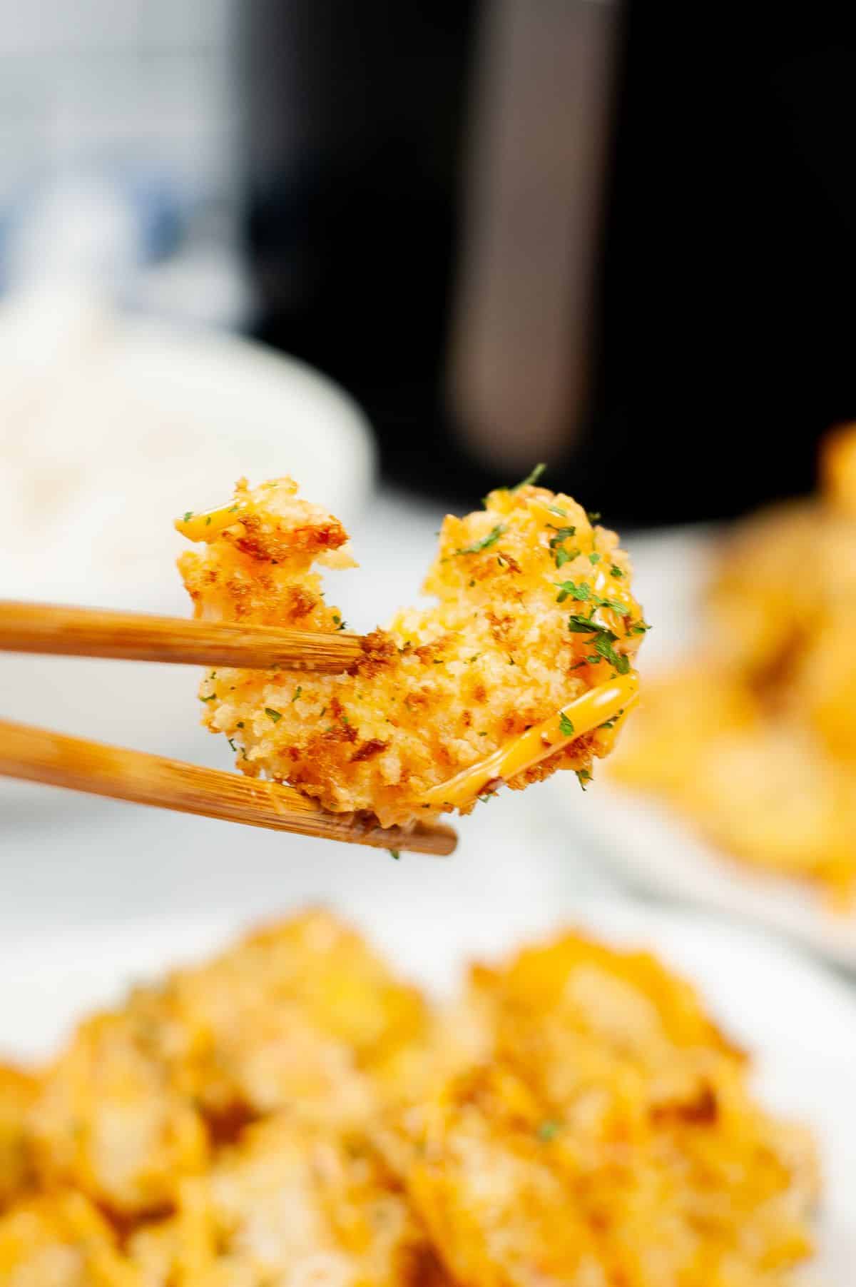 close up of piece of bang bang shrimp being held by chopsticks