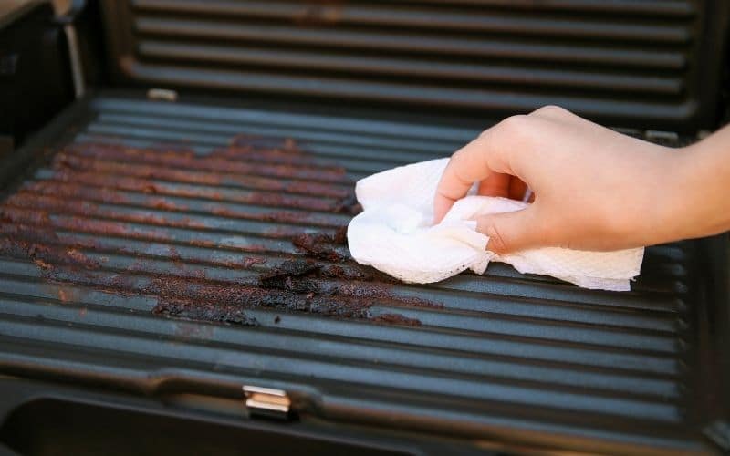 a hand using a white cloth to clean a grill