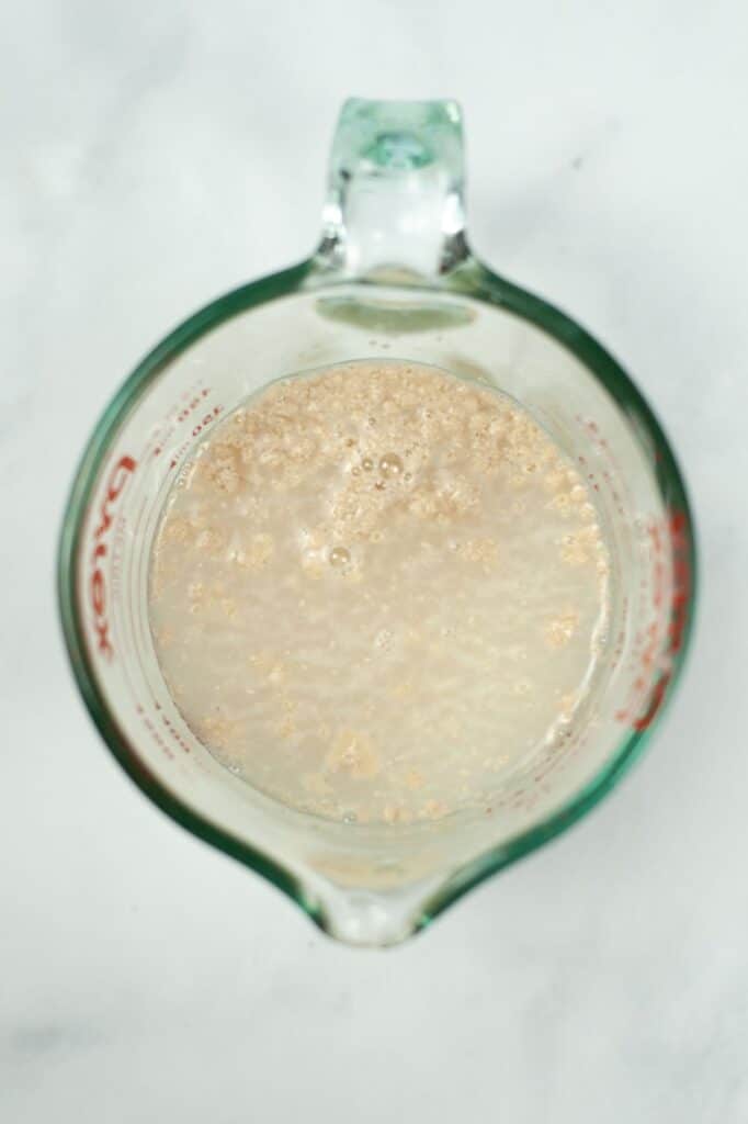 a glass measuring cup with water, sugar and yeast in it
