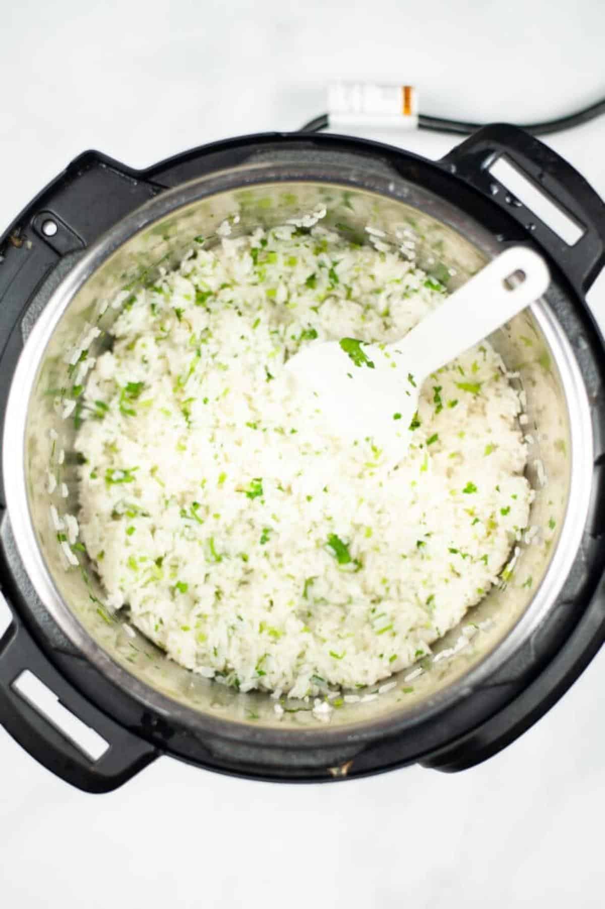 A white spoon in the instant pot to stir the copycat cilantro lime rice.