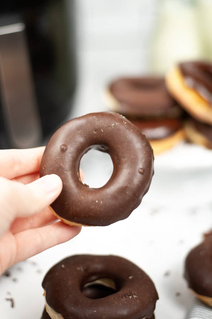 hand holding a chocolate glazed donut with more donuts in the background 