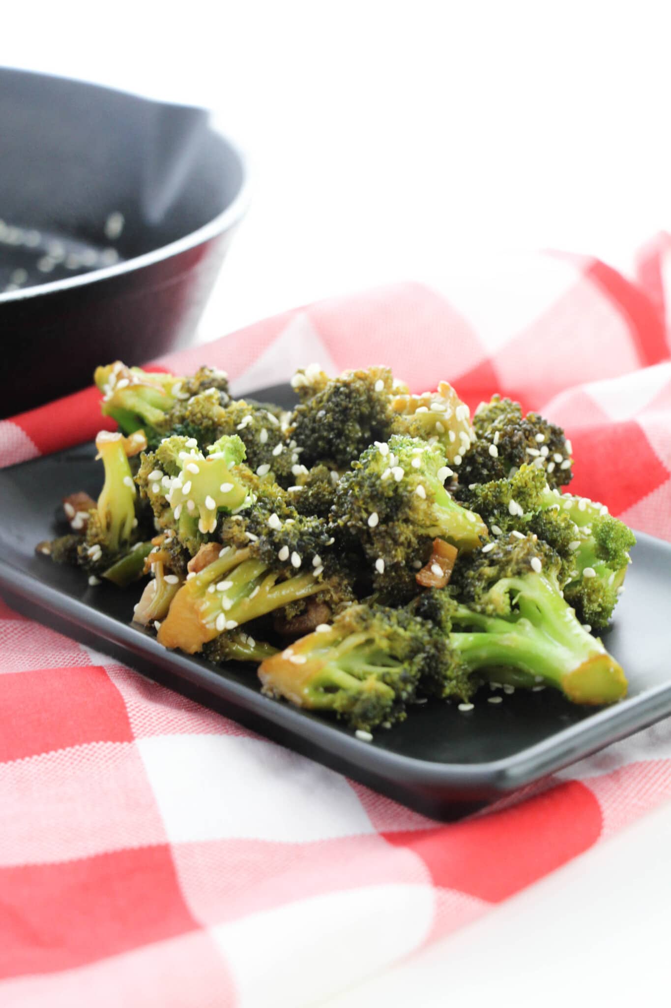black plate full of Asian Style Broccoli on red and white tablecloth 