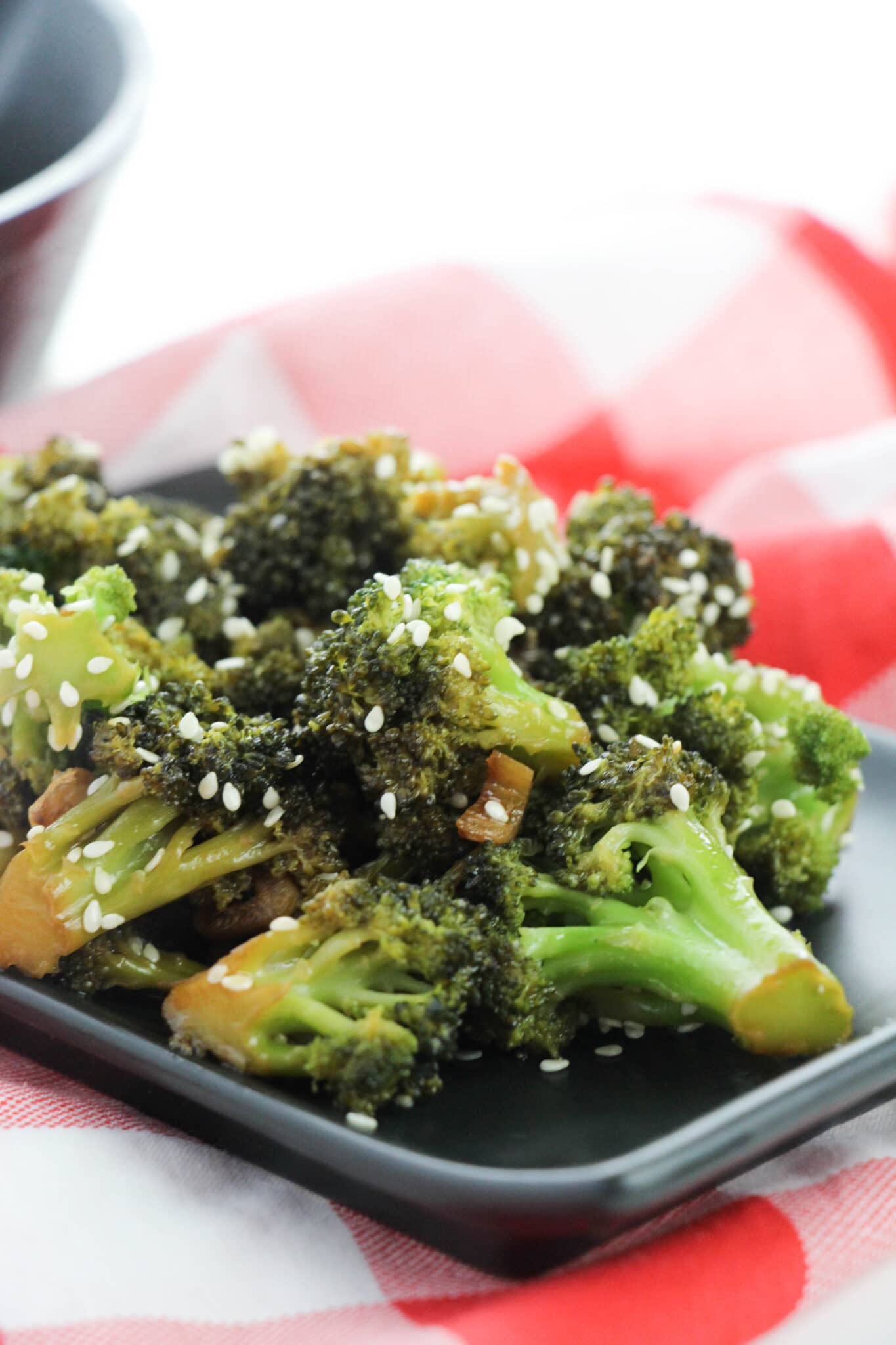 black plate full of Asian Style Broccoli on red and white tablecloth 
