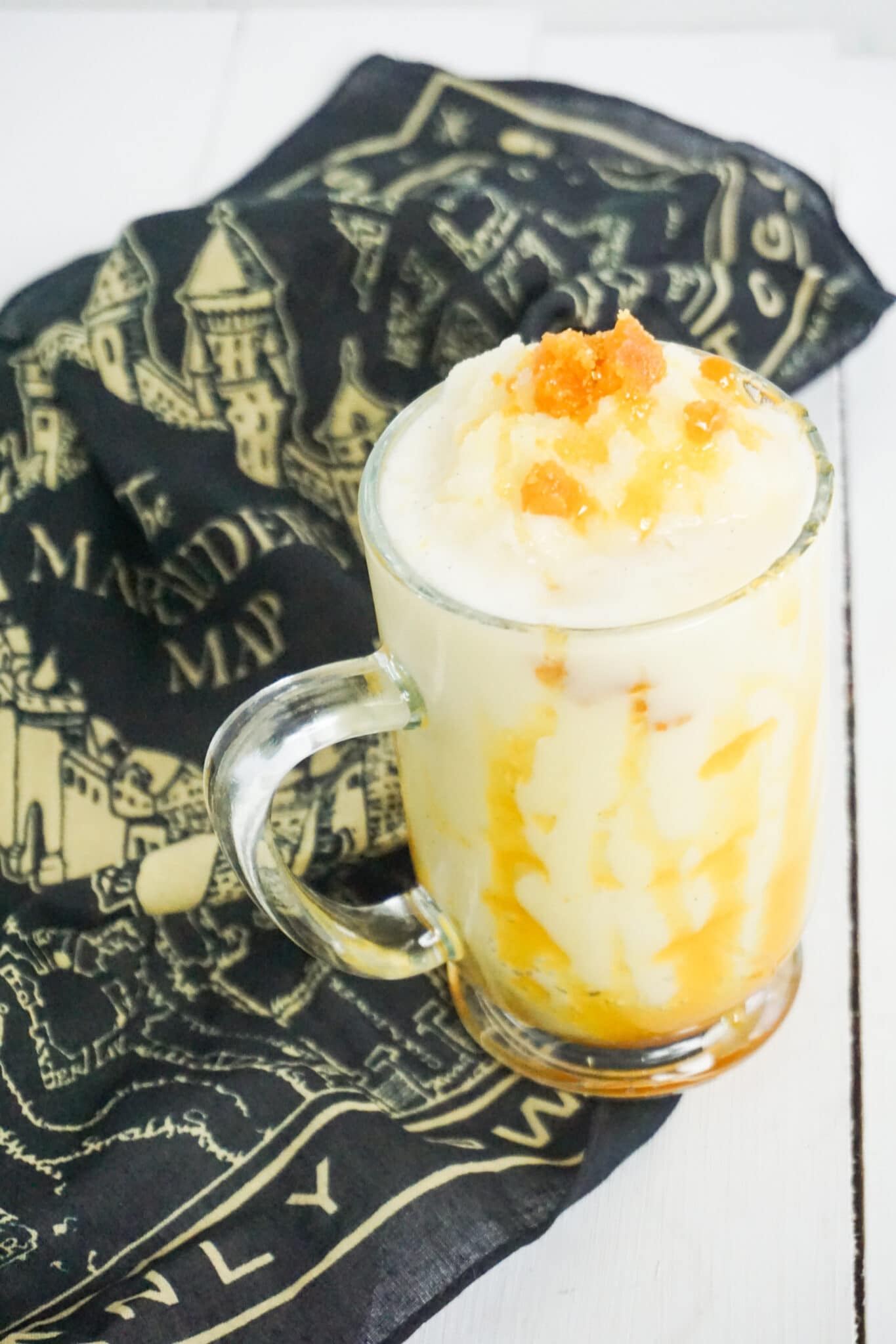 homemade butterbeer frappuccino in a glass next to a black and yellow cloth