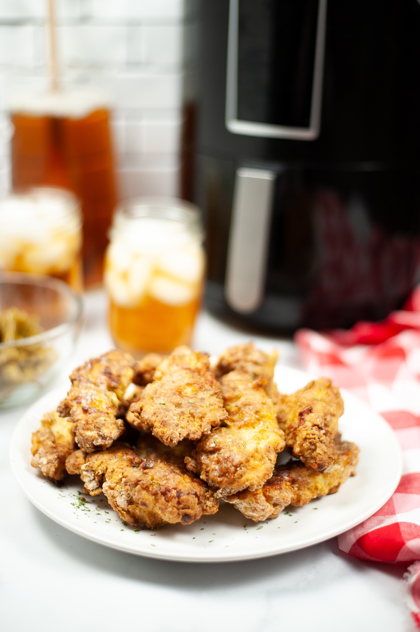 air fryer chicken tenders on a white plate with a glass of iced tea and an air fryer in the background