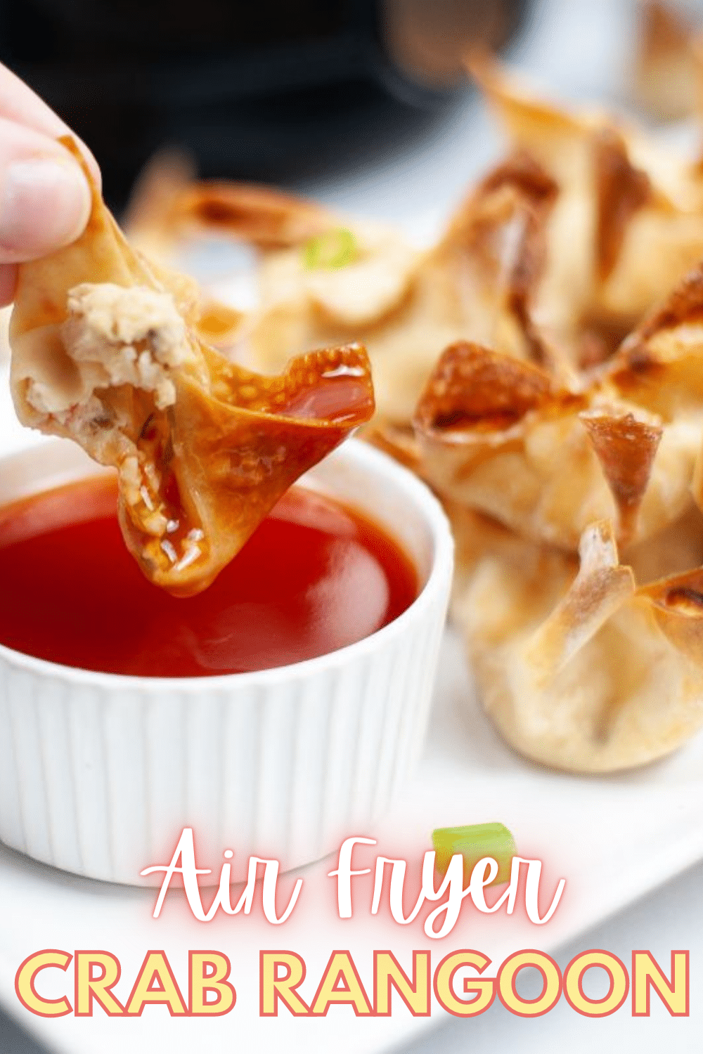 A piece of Air Fryer Crab Rangoon being dipped in a red sauce with the rest of the pieces on a plate