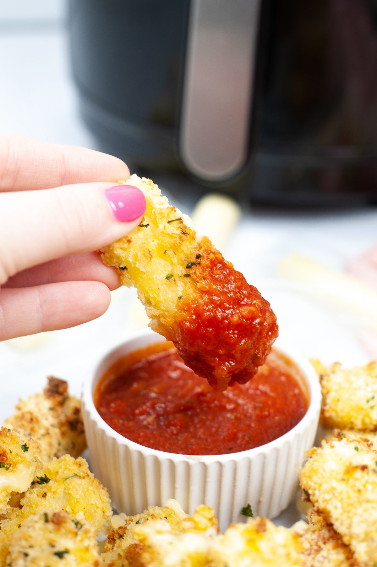 A piece of mozzarella stick being dipped in a red sauce.