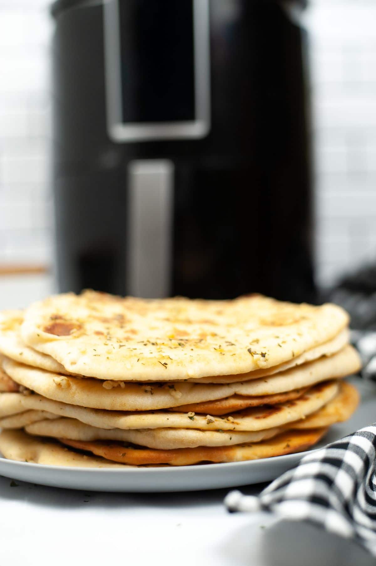 A stack of Air Fryer Naan viewed from its side, highlighting the tiny bits of garlic and parsley garnish.