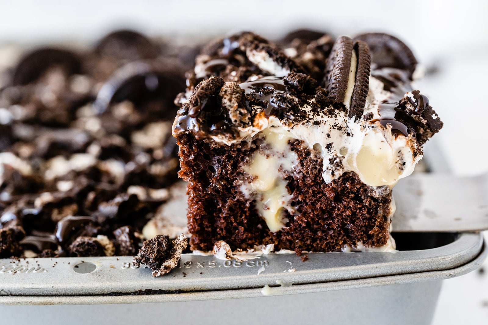 close up of a piece of Oreo poke cake with more cake in a pan in the background