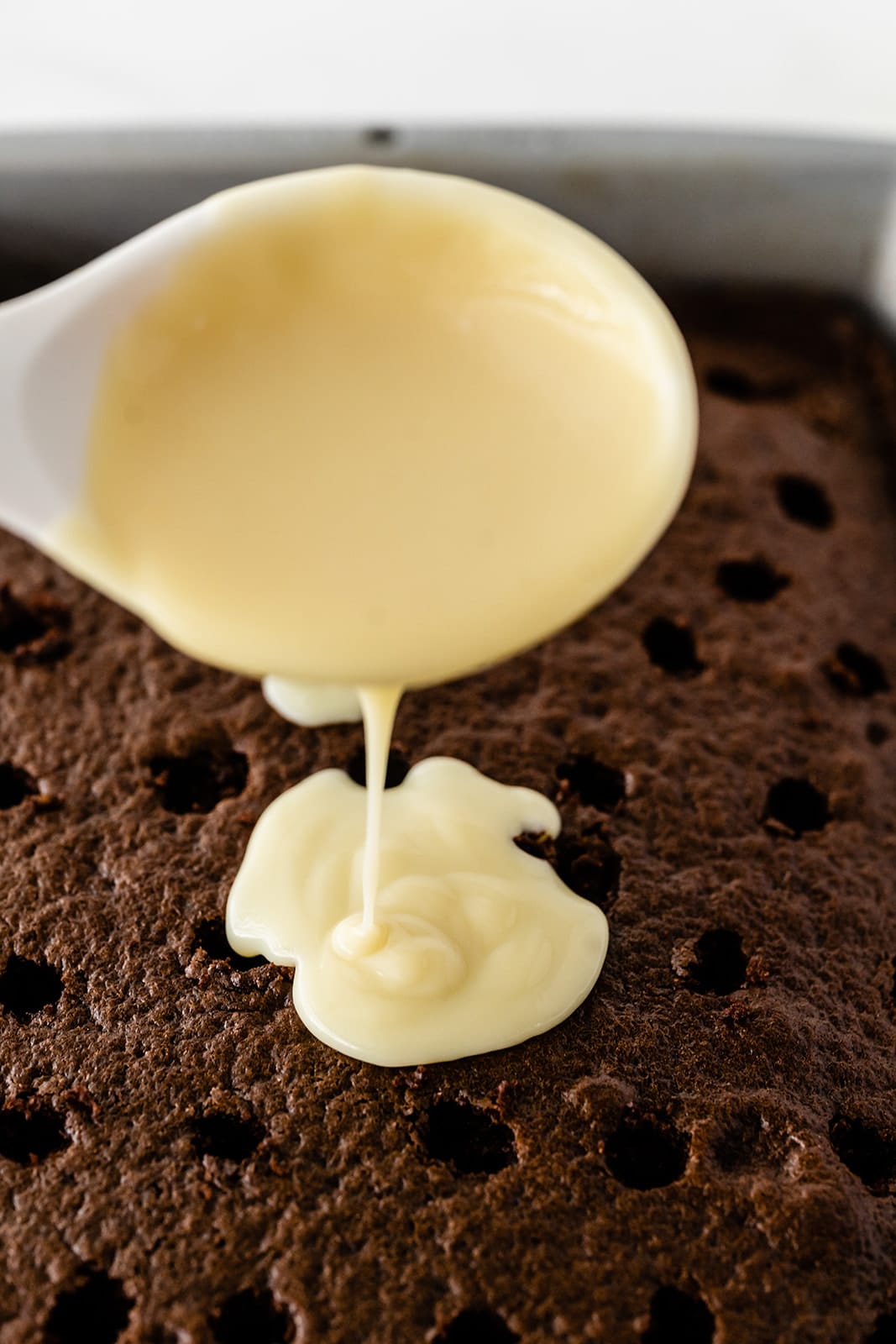 pudding being poured from a spoon into the holes of a chocolate cake