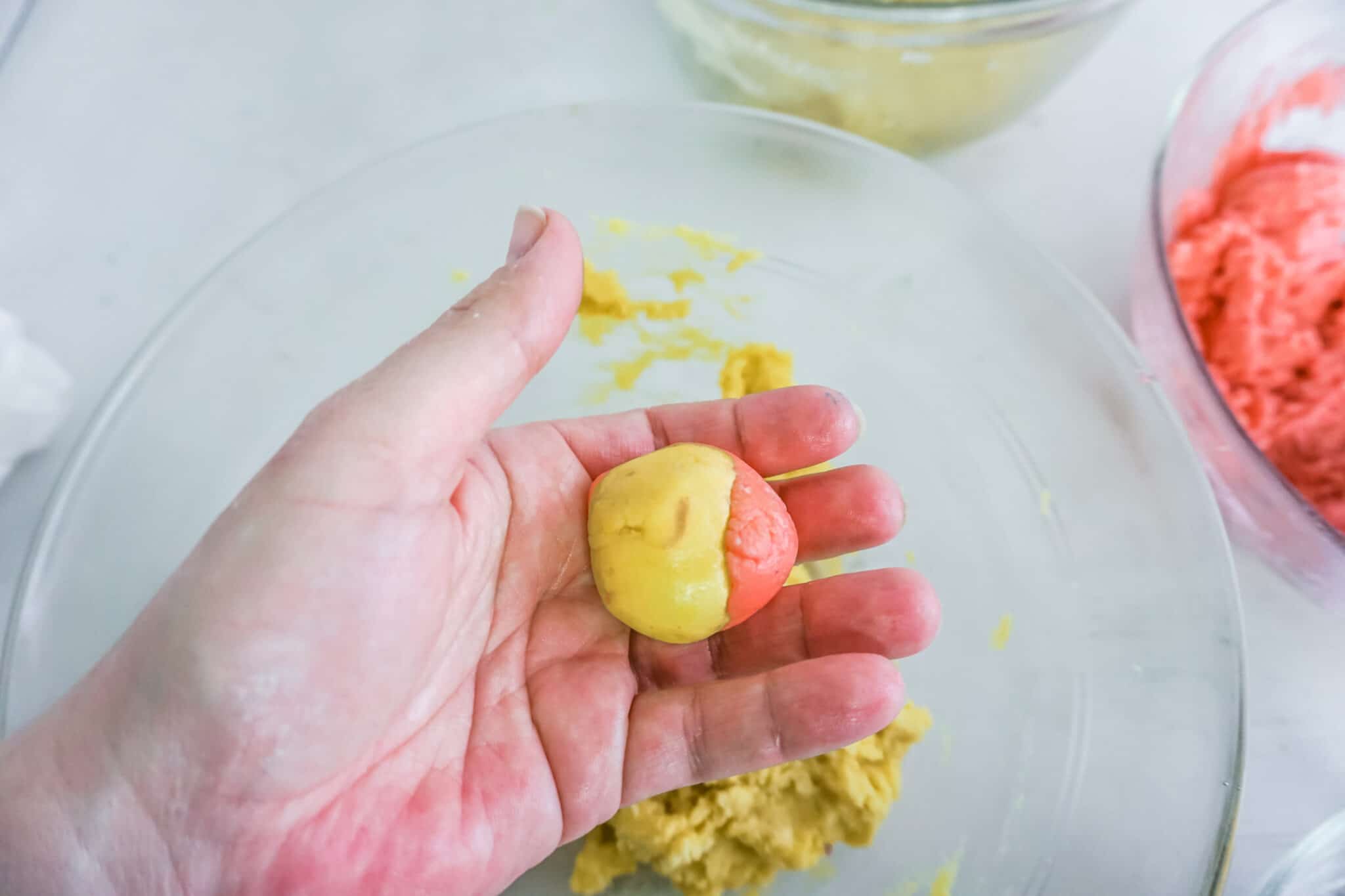 a hand holding strawberry and lemonade cake dough mixed together in a ball over a bowl of cake mix in a glass bowl