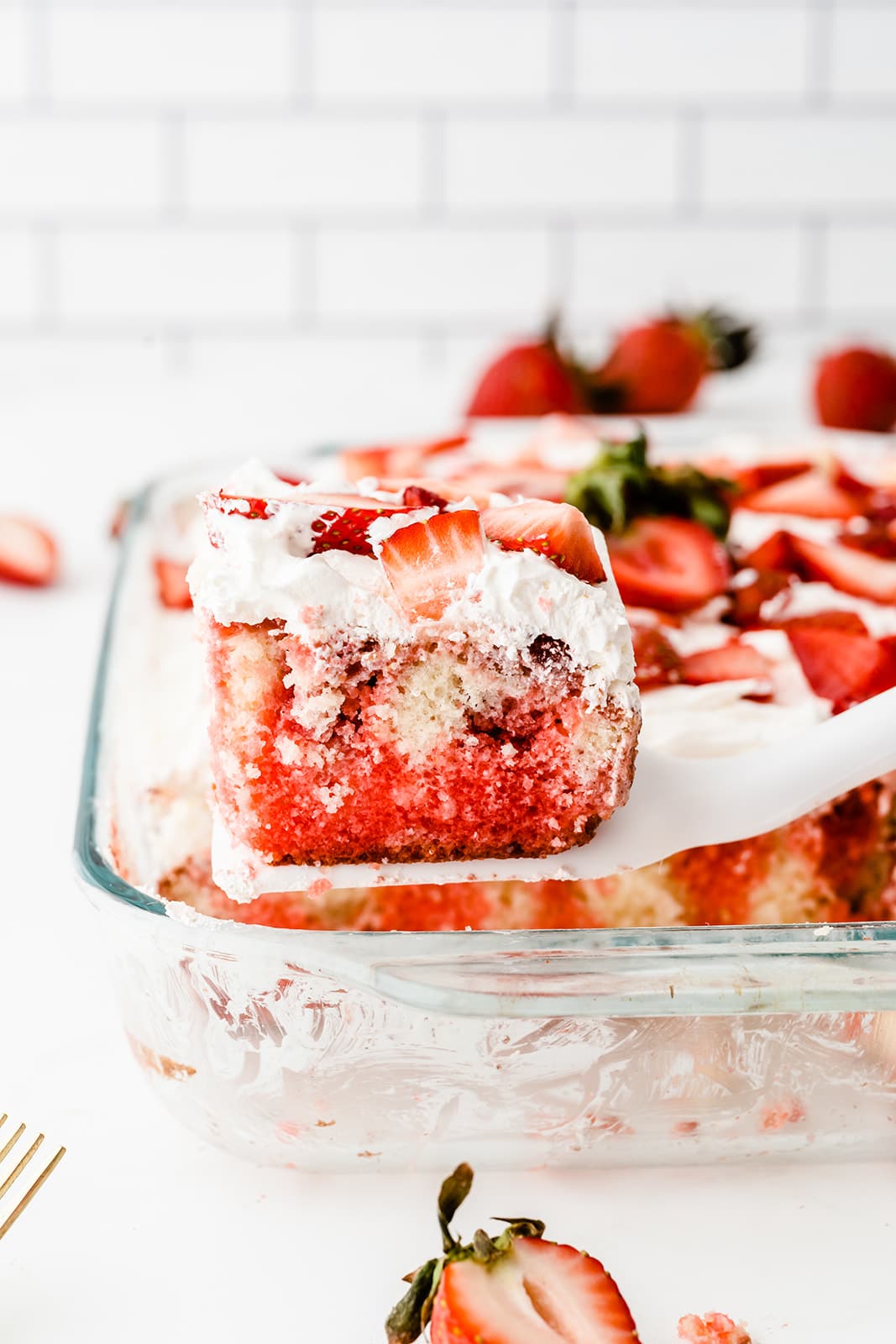 piece of Strawberry Poke Cake on a spatula above the rest of the cake in a glass dish