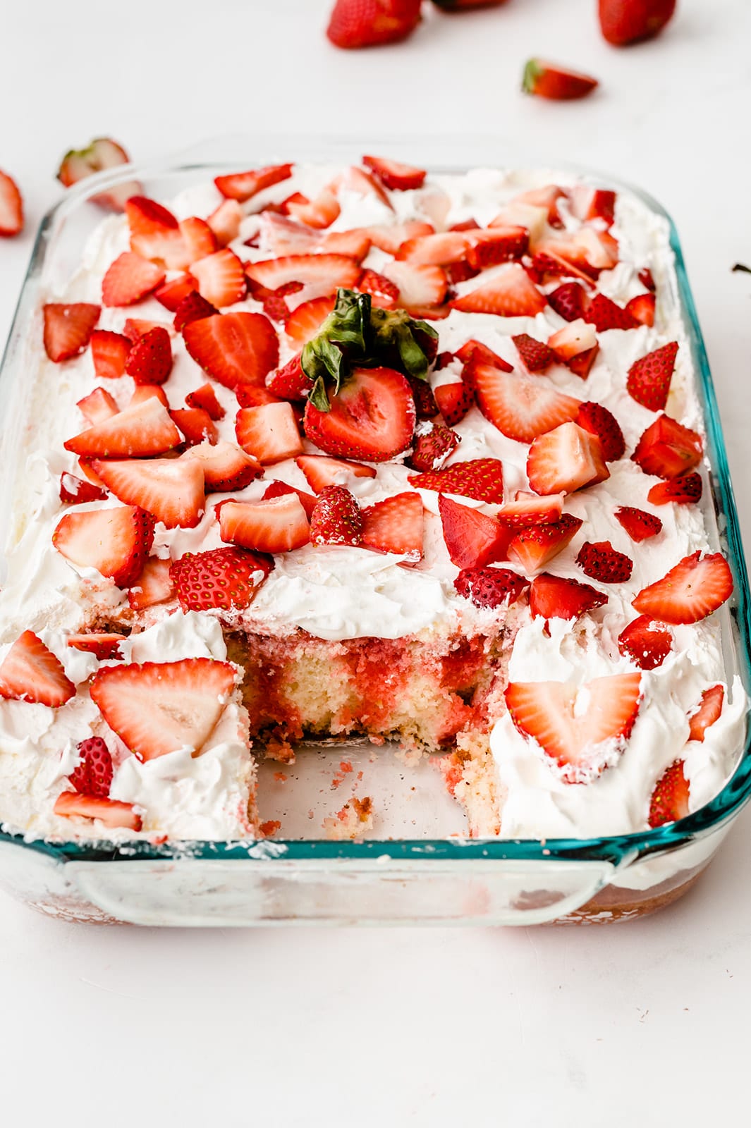cake pan full of strawberry poke cake with one piece missing 