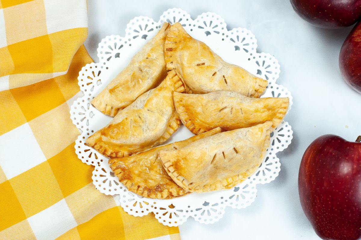 A horizontal overhead shot of Air Fryer Caramel Apple Empanadas on a white serving plate with some apples on the right side of the frame