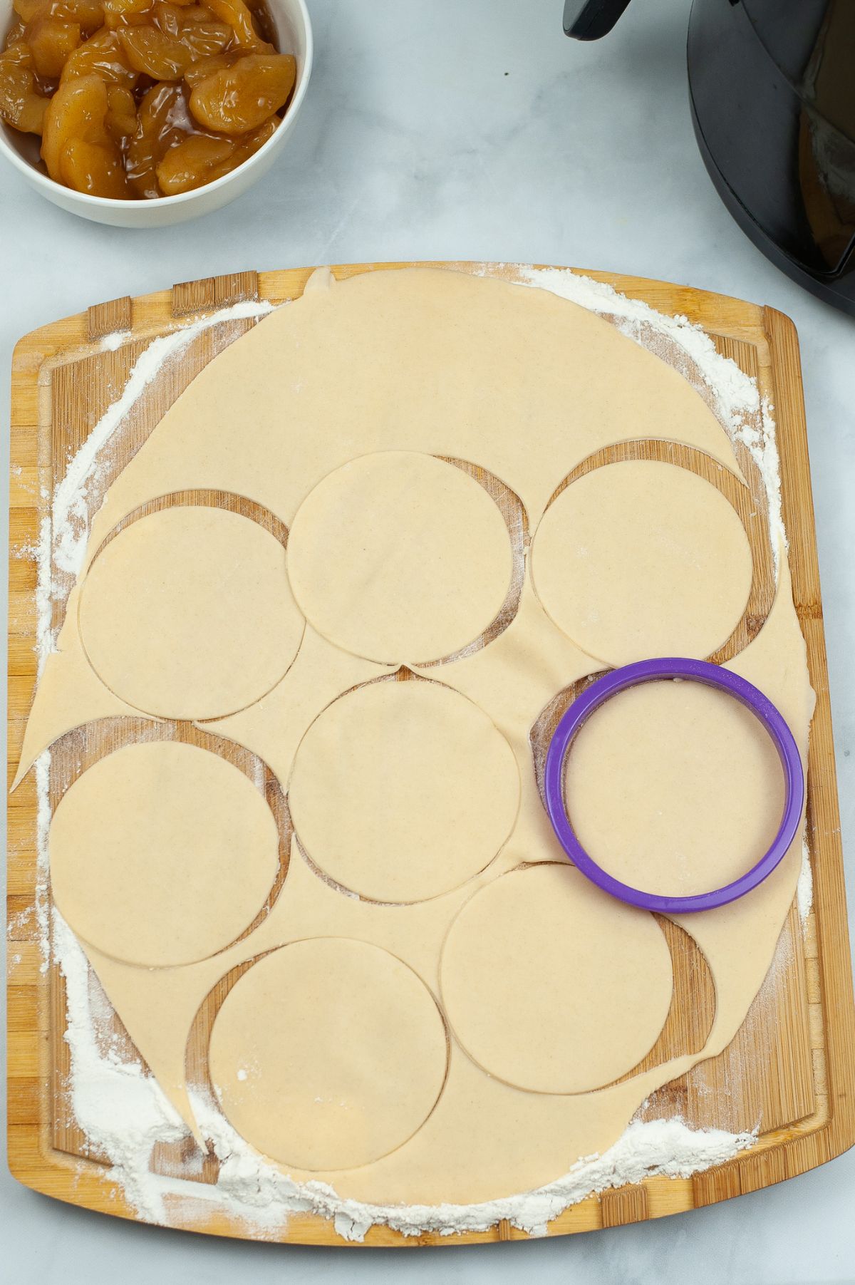 A flattened pie crust on a wooden chopping board being cut out to form circle for the pies.