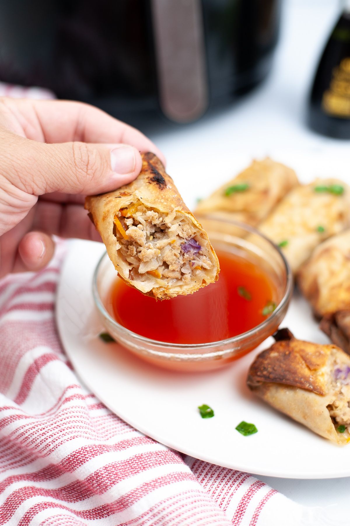 A hand holding a piece of Air Fryer Chicken Egg Roll, ready to be dipped in a sauce.