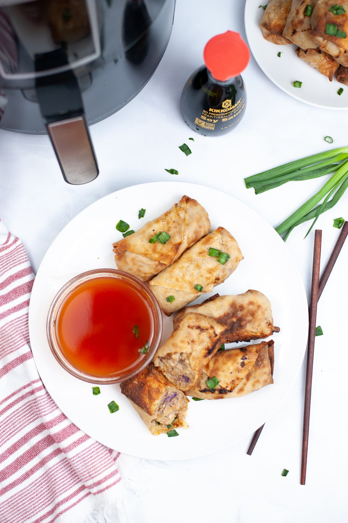 A vertical overhead image of Air Fryer Chicken Egg Rolls on a white serving plate, with egg roll sauce and chopsticks beside the plate.