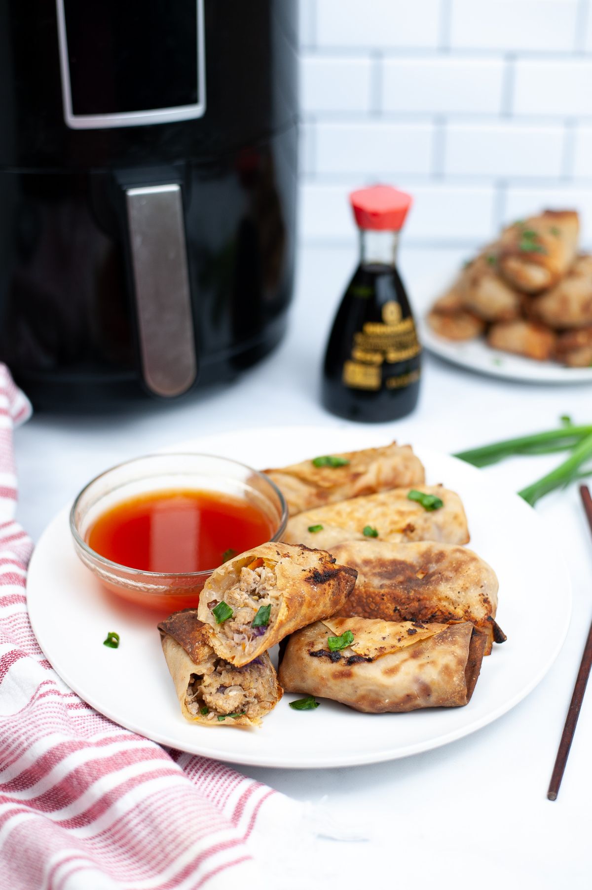Air Fryer Chicken Egg Rolls on a white serving plate, with egg roll sauce, and with one egg roll halved to show the meat inside.