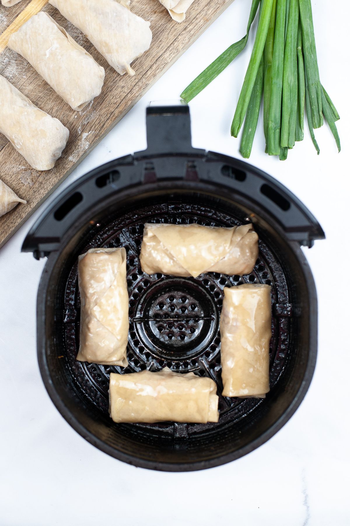 4 egg rolls in an air fryer basket, sprayed with oil and ready to be air fried.