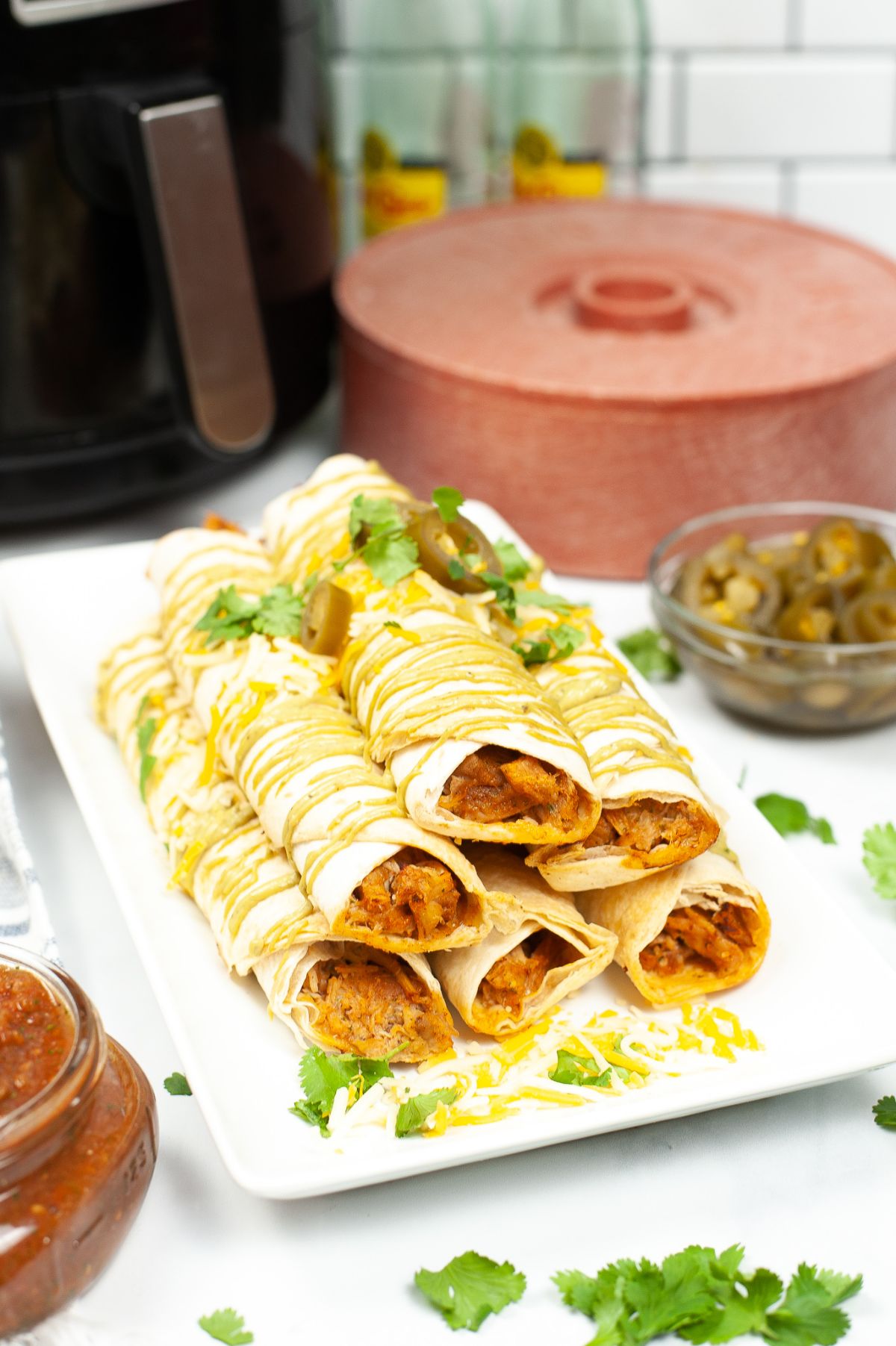 Air Fryer Chicken Taquitos stacked in pyramid-like style on a white rectangular serving plate.