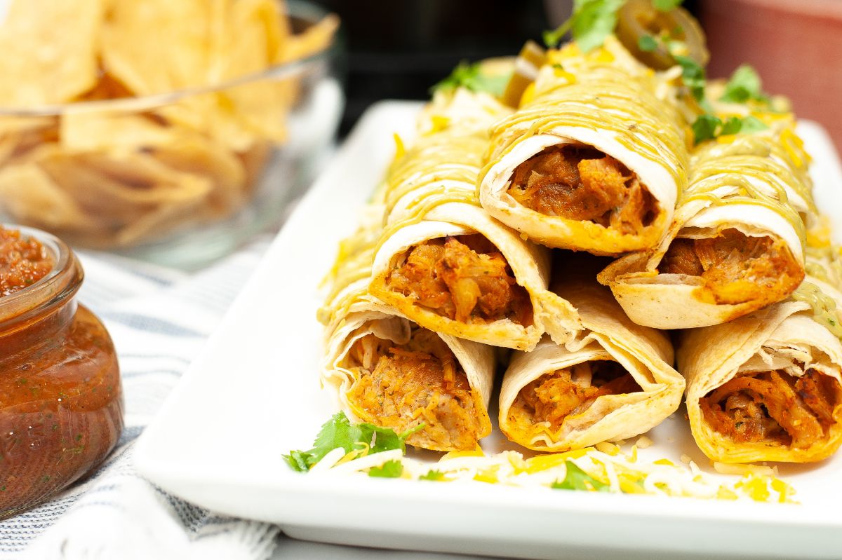 A horizontal image of Air Fryer Chicken Taquitos highlighting the chicken inside the tortilla wrap.