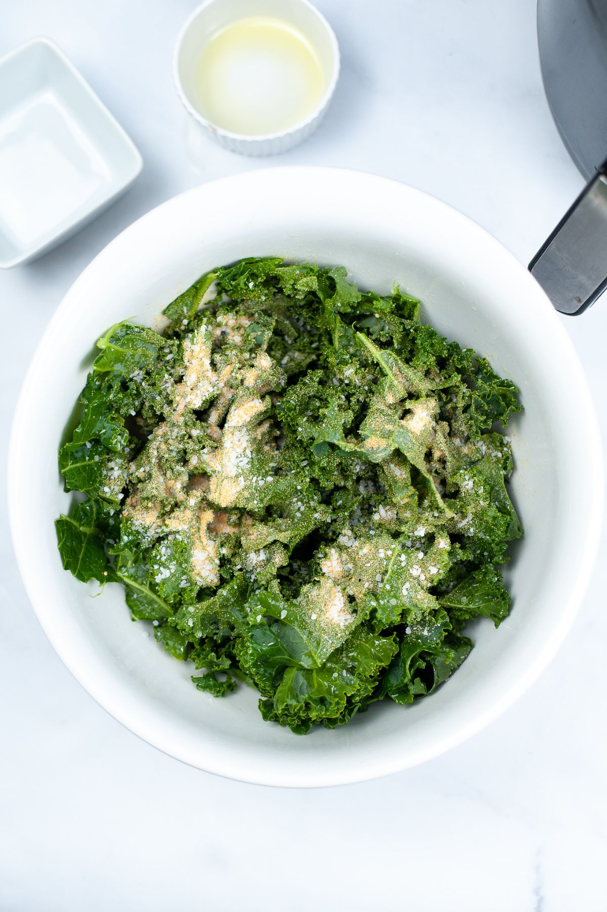 Kale leaves in a bowl seasoned with garlic powder and salt.