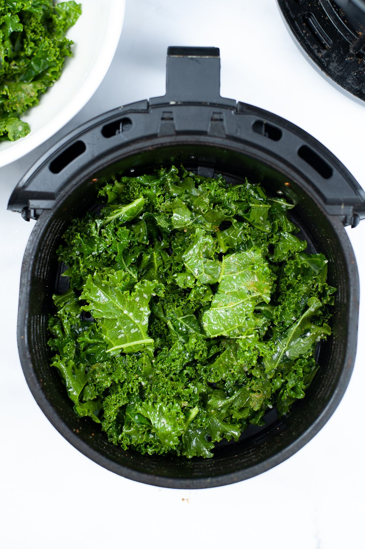 Seasoned Kale leaves in an air fryer basket ready for cooking.