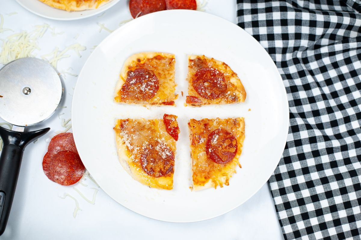A horizontal overhead shot of an Air Fryer Naan Bread Pizza, sliced into 4 pieces, on a white serving plate.